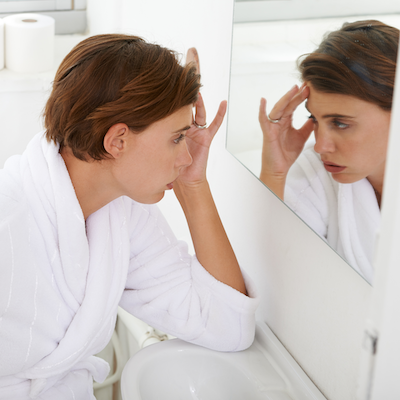 worried woman looks at herself in a mirror