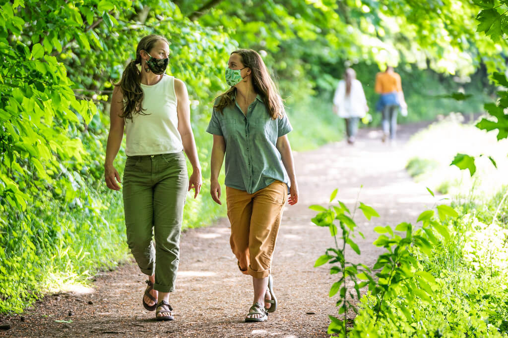 two women walking in a park wearing masks