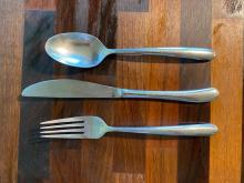 a spoon, fork, and knife lined up horizontally on a wooden counter